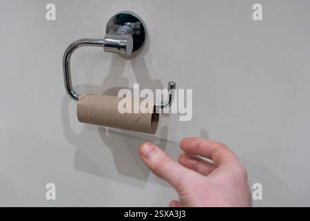 Aman's hand reaching out for an empty toilet roll, UK. Concept: run out, no toilet paper, loo roll, bog roll, none left, caught short, empty roll Stock Photo