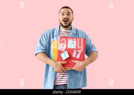 Portrait of surprised young man holding folders with question marks on pink background Stock Photo
