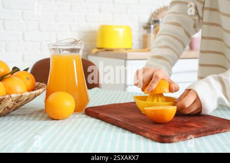 Woman with juicer squeezing fresh oranges in kitchen Stock Photo