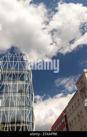 A contemporary glass building featuring a wavy metal facade against a bright sky filled with beautiful clouds, symbolizing architectural innovation an Stock Photo