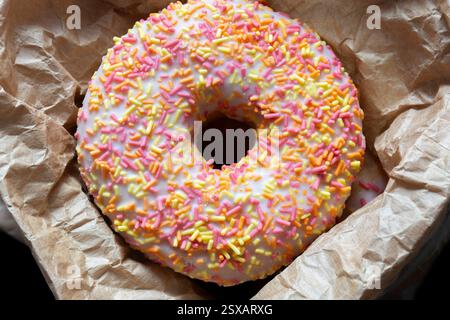 Iced ring doughnuts sprinkled with hundreds and thousands in a brown paper bag. Recycling eco friendly biodegradable packaging Stock Photo
