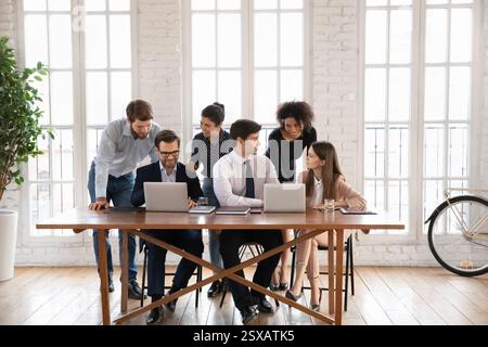 Diverse group of six professionals gathered around table with laptops Stock Photo