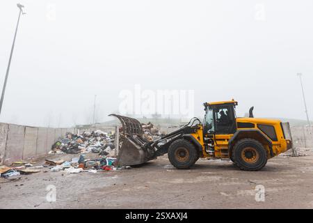 Yellow wheel loader, with lifted scrap grapple, moving along the ...