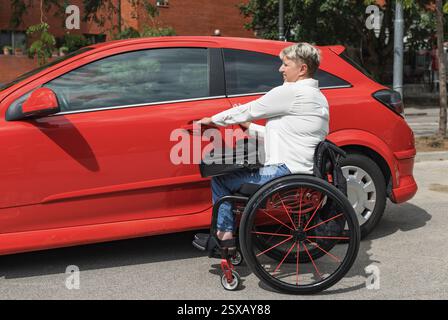 Businesswoman, a driver with a disability getting into a red car. Transport, driving, and physical impairment concepts. Stock Photo