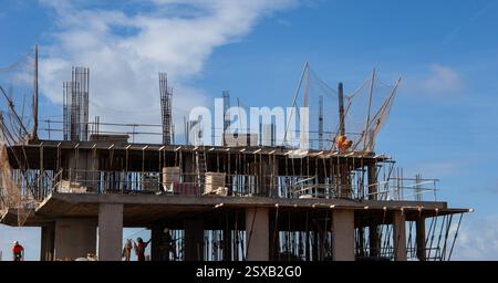 Construction workers and scaffolding on a partially built structure against a blue sky backdrop on a sunny day Costa Teguise Lanzarote Stock Photo