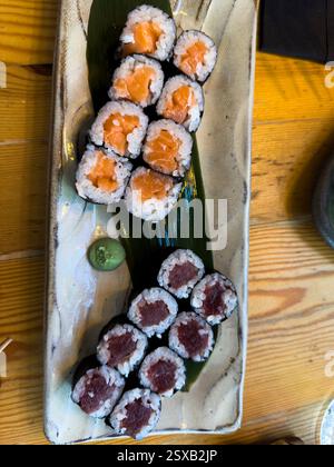 Two sets of hosomaki, one with salmon and one with tuna, served on a rectangular plate with a side of wasabi Stock Photo