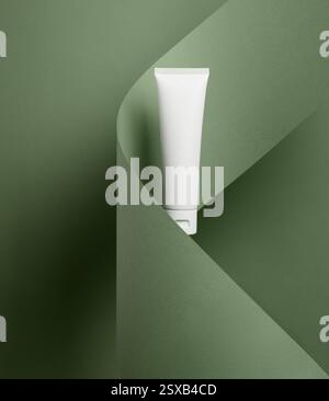 A minimalist white cosmetic tube mockup is elegantly presented against a modern green folded paper background for a chic and stylish look Stock Photo