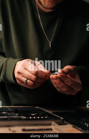Vertical cropped shot of electronic engineer using tweezers, fixing components on laptop motherboard, performing maintenance and troubleshooting in Stock Photo