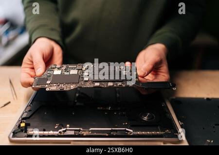 Electronic technician carefully handling delicate computer motherboard during precision laptop repair at professional workbench. Stock Photo