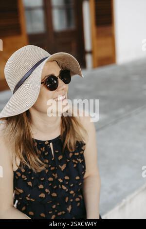 Woman with sunglasses and sun hat sitting on stone steps Stock Photo