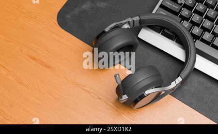 Overhead shot of black headphones resting on wooden desk beside computer keyboard, home office workspace, high-quality audio gear, modern tech setup Stock Photo