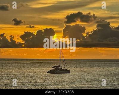 Golden Sunset Over the Dark Sea with a Catamaran on the Horizon The sun, hidden behind thick clouds just above the sea, casts a golden-orange glow Stock Photo