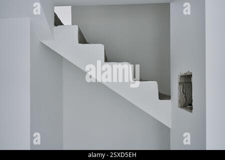 Unfinished concrete staircase in modern minimalist interior. New apartment with raw construction elements and white walls. Building under repair Stock Photo