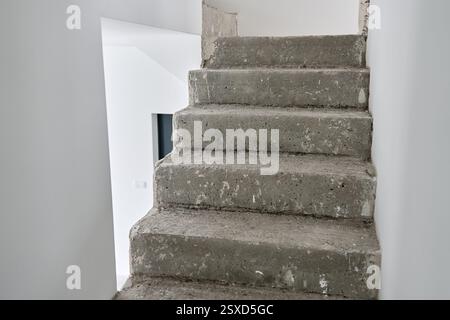 Unfinished concrete staircase in modern minimalist interior. New apartment with raw construction elements and white walls. Building under repair Stock Photo