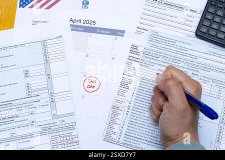 A close-up shot of a hand gripping a pen over IRS tax forms, with a calendar highlighting April 15, 2025, as Tax Day. The image represents the stress Stock Photo