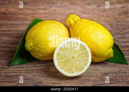 3 Lemons with green leaves on wooden table Stock Photo