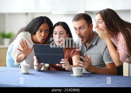 Amazed interracial group of friends checking tablet content in the kitchen at home Stock Photo