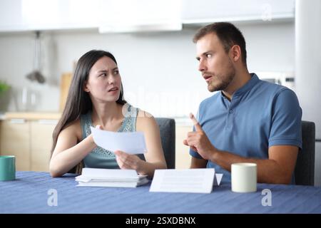 Woman holding bill scolding her partner who denies accusation in the kitchen at home Stock Photo