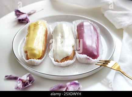 Three eclairs with different fillings lie in a plate Stock Photo