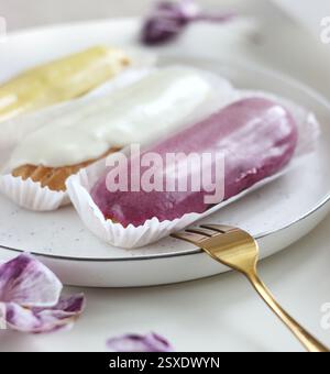 Three eclairs with different fillings lie in a plate on the table Stock Photo