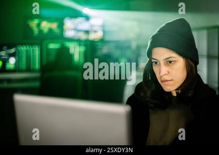 Female young hacker working on computer in dark room programming code Stock Photo