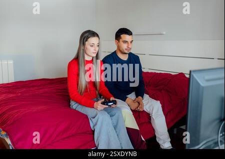 Young couple playing video games in bedroom using wireless controller Stock Photo
