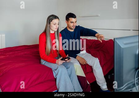 Young couple playing video games in bedroom using wireless controller Stock Photo