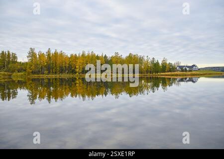 Autumn colors reflecting on calm lake with farmhouse in background Stock Photo