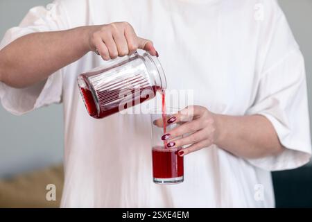 Woman pouring red juice from a jug into a glass, closeup Stock Photo