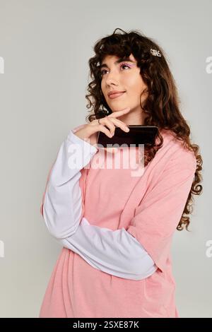 A fashionable young woman gazes thoughtfully while holding her smartphone, radiating emotion. Stock Photo