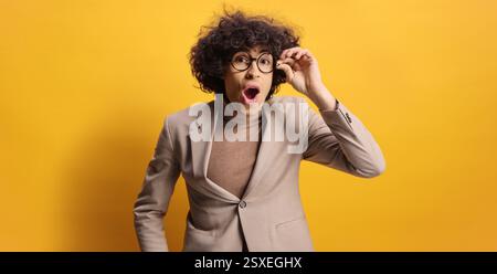 Surprised young man looking through glasses against a yellow background Stock Photo
