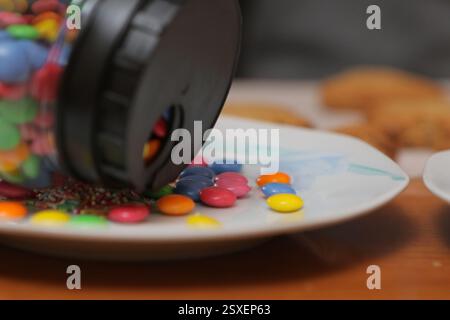 Colorful chocolate buttons spilling from a jar onto a plate, creating a sweet and tempting treat Stock Photo
