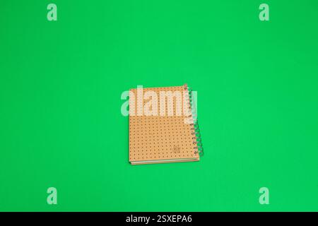 Closed spiral notebook with dotted cover placed on a vivid green backdrop, creating a simple yet striking visual Stock Photo