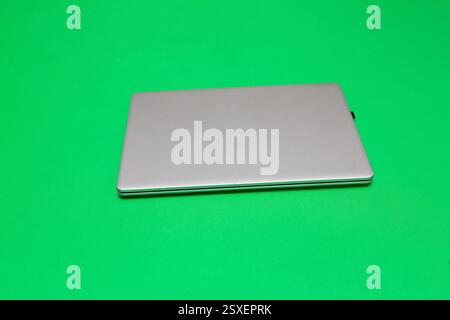 Closed laptop on a vibrant green background, ready for chroma keying and visual effects Stock Photo