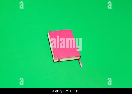 Pink notebook with bookmark lying on a vibrant green screen backdrop, ideal for chroma keying and creative projects Stock Photo