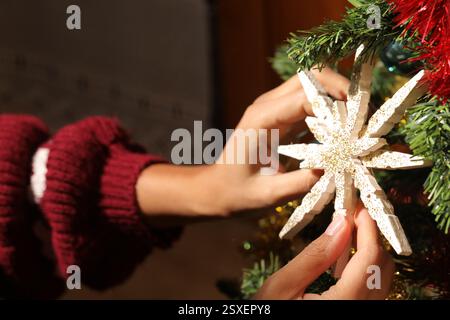 Hands decorating christmas tree with a beautiful white and gold snowflake ornament, adding festive touch to holiday preparations Stock Photo