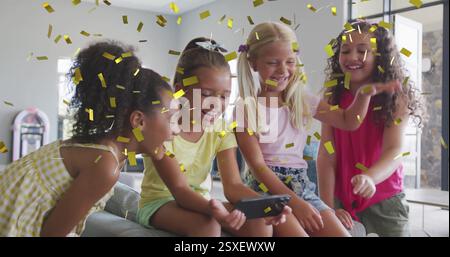 Image of gold confetti over happy diverse schoolgirls using smartphone and laughing in classroom Stock Photo