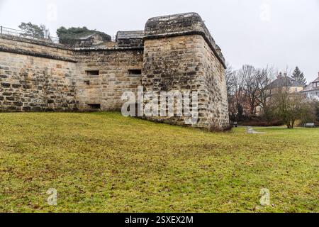 The corner of a sandstone bastion of the historic fortification shows narrow embrasures in its masonry, with a lawn stretching out behind it and residential houses in the background. The bastion is part of the town fortification, expanded from the medieval city wall along Italian lines from 1553, after Forchheim was captured during the Second Margrave War in 1552; the fortress was considered one of the strongest in the Prince-Bishopric of Bamberg during the Thirty Years' War. About a third of the original fortification survives today. Karolingerstraße, Forchheim, Bavaria, Germany. Stock Photo
