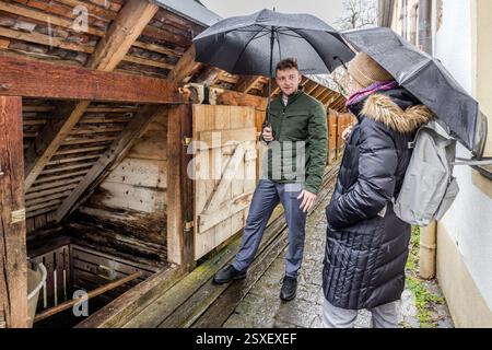 Anton Karnbaum talks under an umbrella with travel journalist Angela Berg in front of the open fish boxes on the Wiesent in Forchheim. The wooden boxes have served Forchheim's fishmongers for centuries to keep fish alive. Wiesentstraße, Forchheim, Bavaria, Germany. Stock Photo