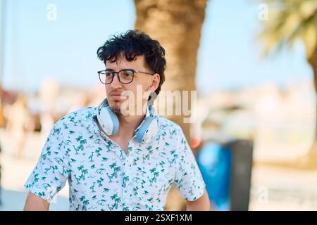 Smiling young man with glasses and headphones in a sunny outdoor setting Stock Photo