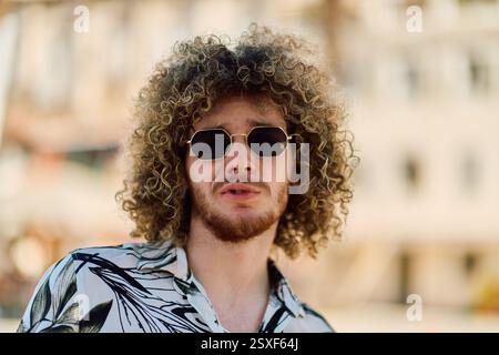 A stylish European man with an Afro hairstyle and sunglasses exudes confidence in a sunlit outdoor setting. Stock Photo