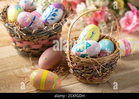 Decorated Easter eggs in a basket with flowers in background on a wooden table Stock Photo