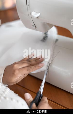 A woman cutting fabric with scissors beside her sewing machine, perfect for DIY, crafting, sewing, and home decor content. Stock Photo