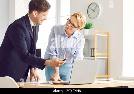 Office male, female positive colleagues working on project at laptop, coworking, typing, talking  Stock Photo