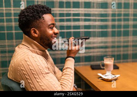 Freelancer is having pause from work, he is talking on smartphone and drinking hot chocolate in bar. Stock Photo