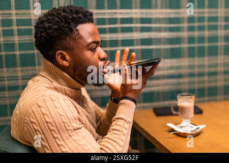 Young man is having pause from work, he is talking on smartphone and drinking hot chocolate in bar. Stock Photo