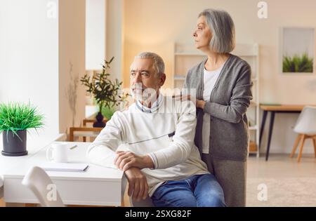 Thoughtful senior couple contemplating decision while looking into distance through window. Stock Photo