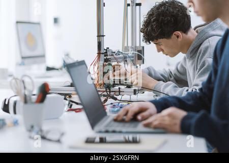 Academic students working on a project in the lab, they are using a laptop and a 3D printer Stock Photo