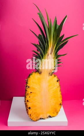 This pineapple, sliced in half, reveals its juicy yellow flesh and detailed texture, set against a bold pink backdrop for a striking visual contrast. Stock Photo
