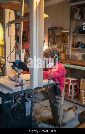 Man woodworker in protective gear shaping stool base on drilling cnc machine in furniture workshop Stock Photo